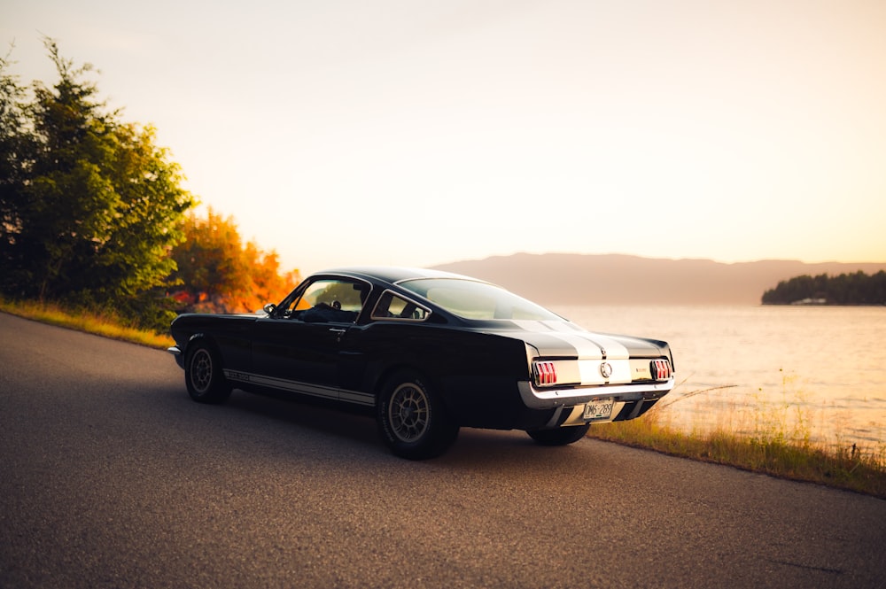 a black car driving down a road next to a body of water