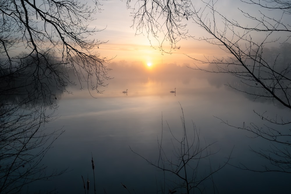 the sun is setting over a foggy lake