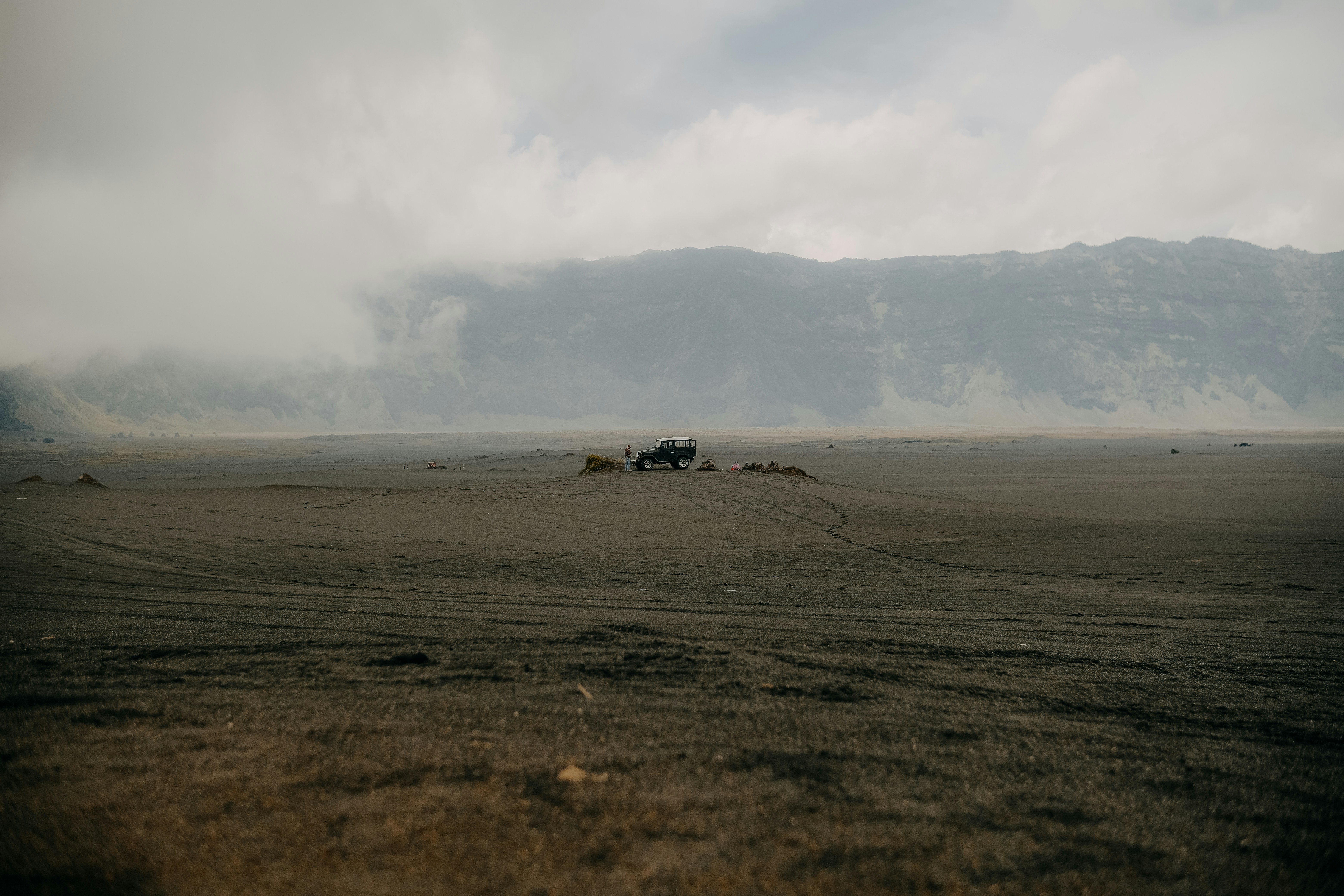 a truck driving through a desert with mountains in the background