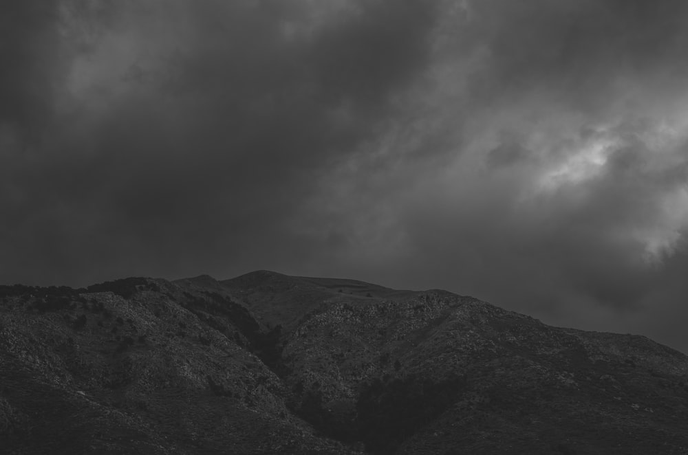 a black and white photo of a mountain under a cloudy sky