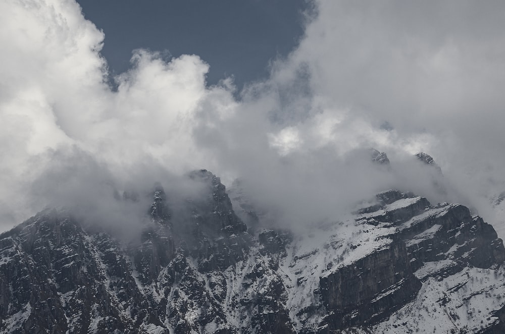 a mountain covered in snow and clouds under a blue sky