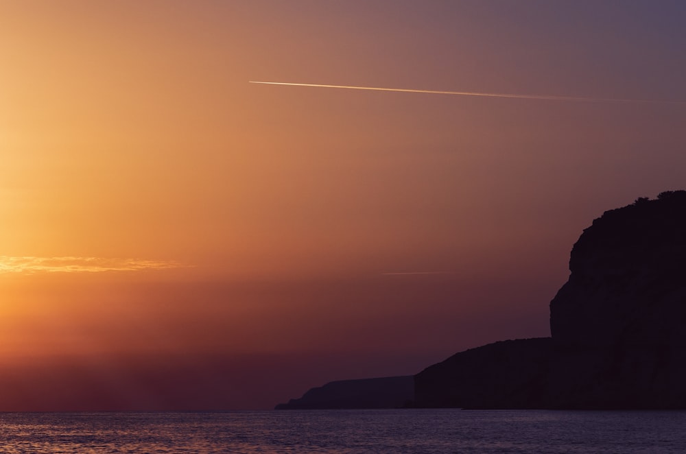 the sun is setting over the ocean with a plane in the sky