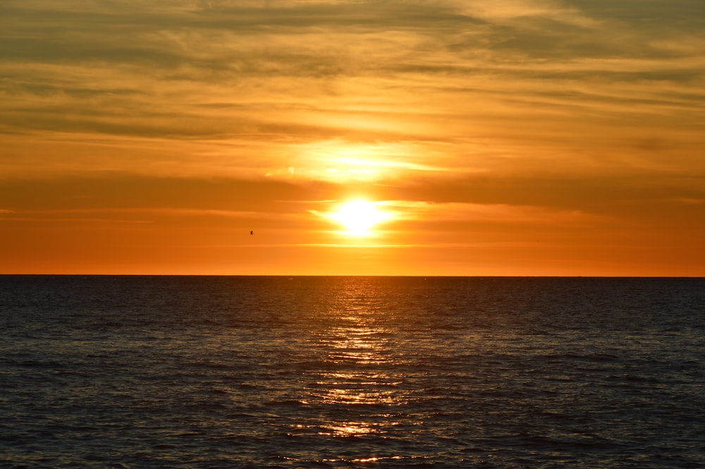 ein großes Gewässer mit einem Sonnenuntergang im Hintergrund