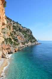 a sandy beach next to a cliff with clear blue water