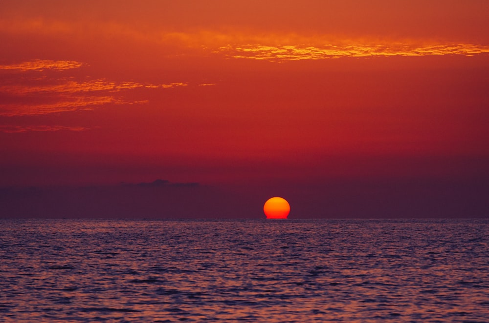 the sun is setting over the ocean on a cloudy day