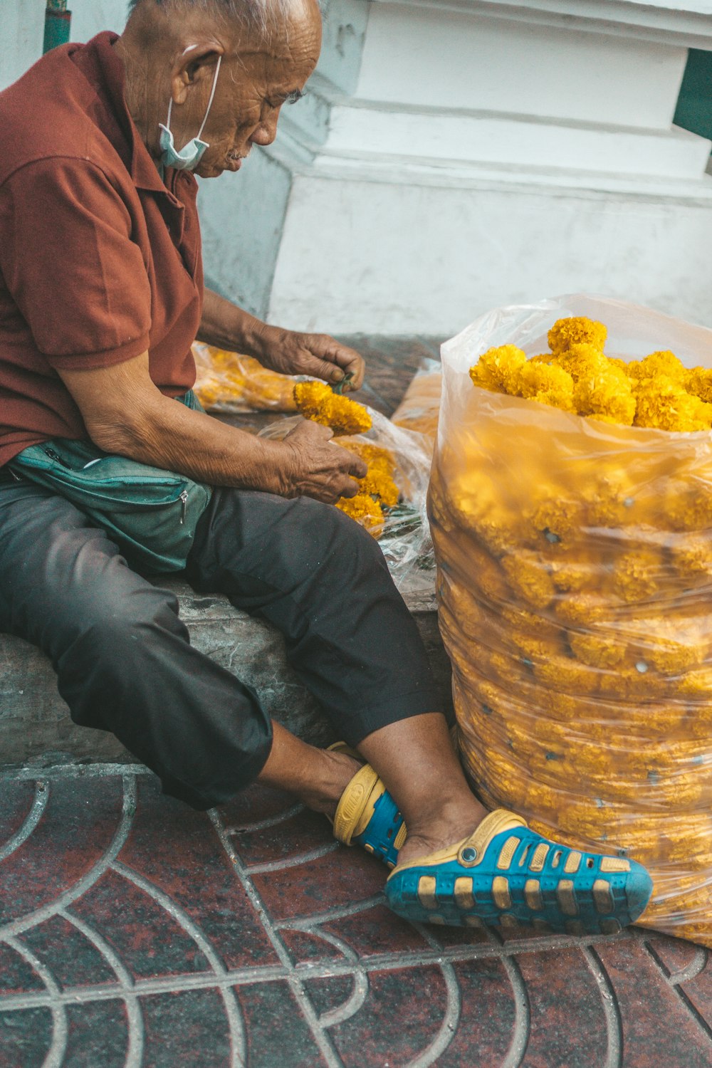 a man sitting on the ground next to a bag of yellow flowers