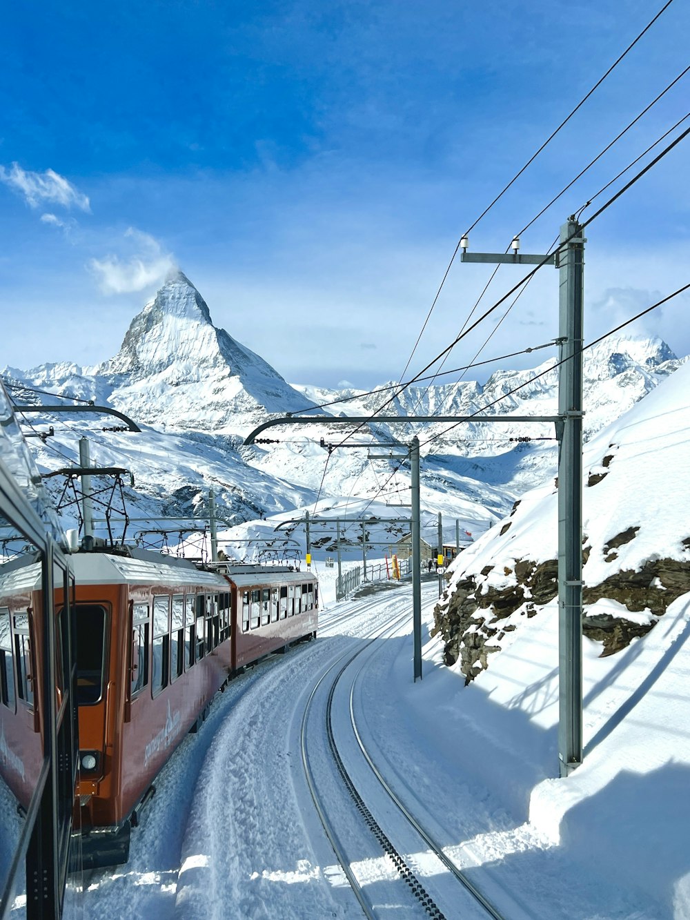 a red train traveling down tracks next to a snow covered mountain