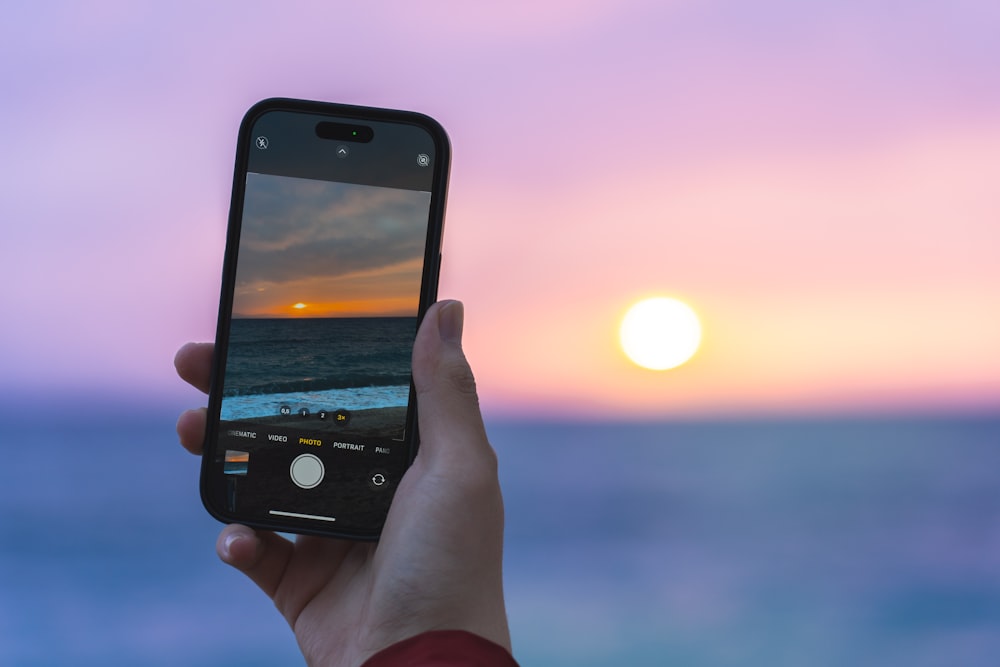 une personne prenant une photo d’un coucher de soleil sur l’océan