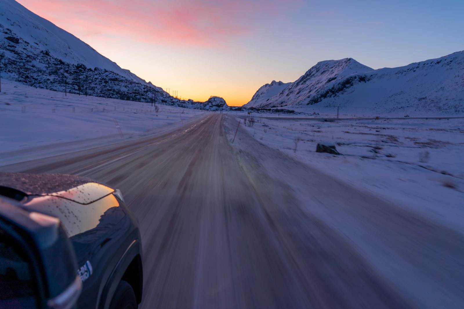 A car follows a snow-covered road beside the sea in Norway