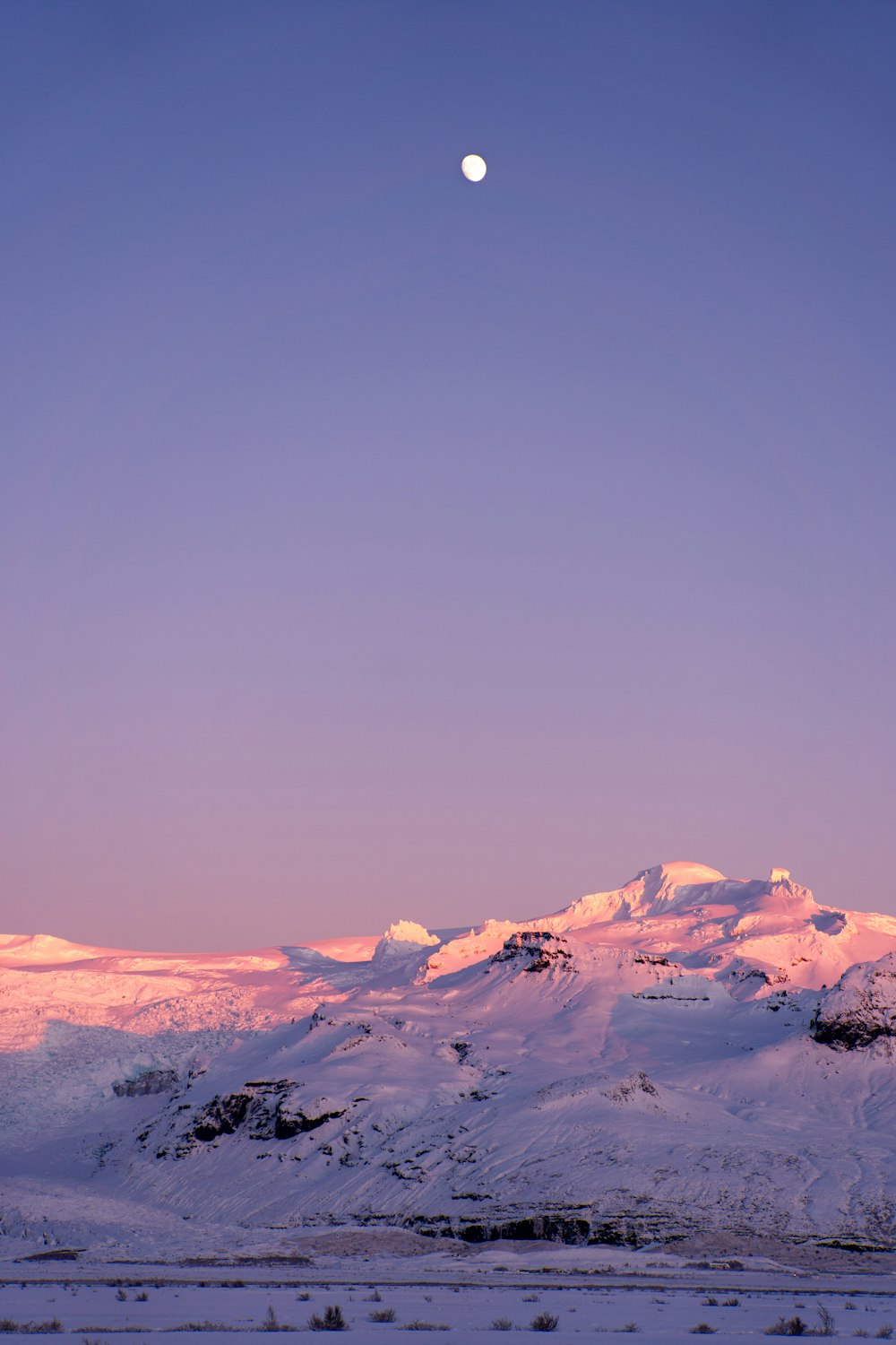 a lua está se pondo sobre uma cordilheira nevada