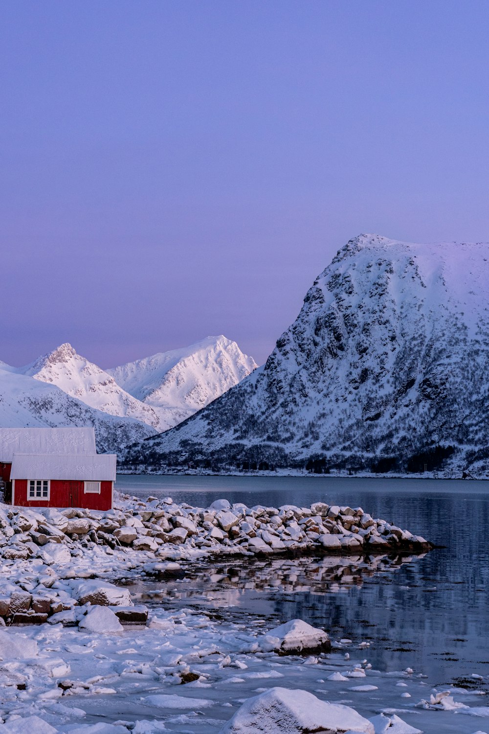 a red house sitting on top of a snow covered shore