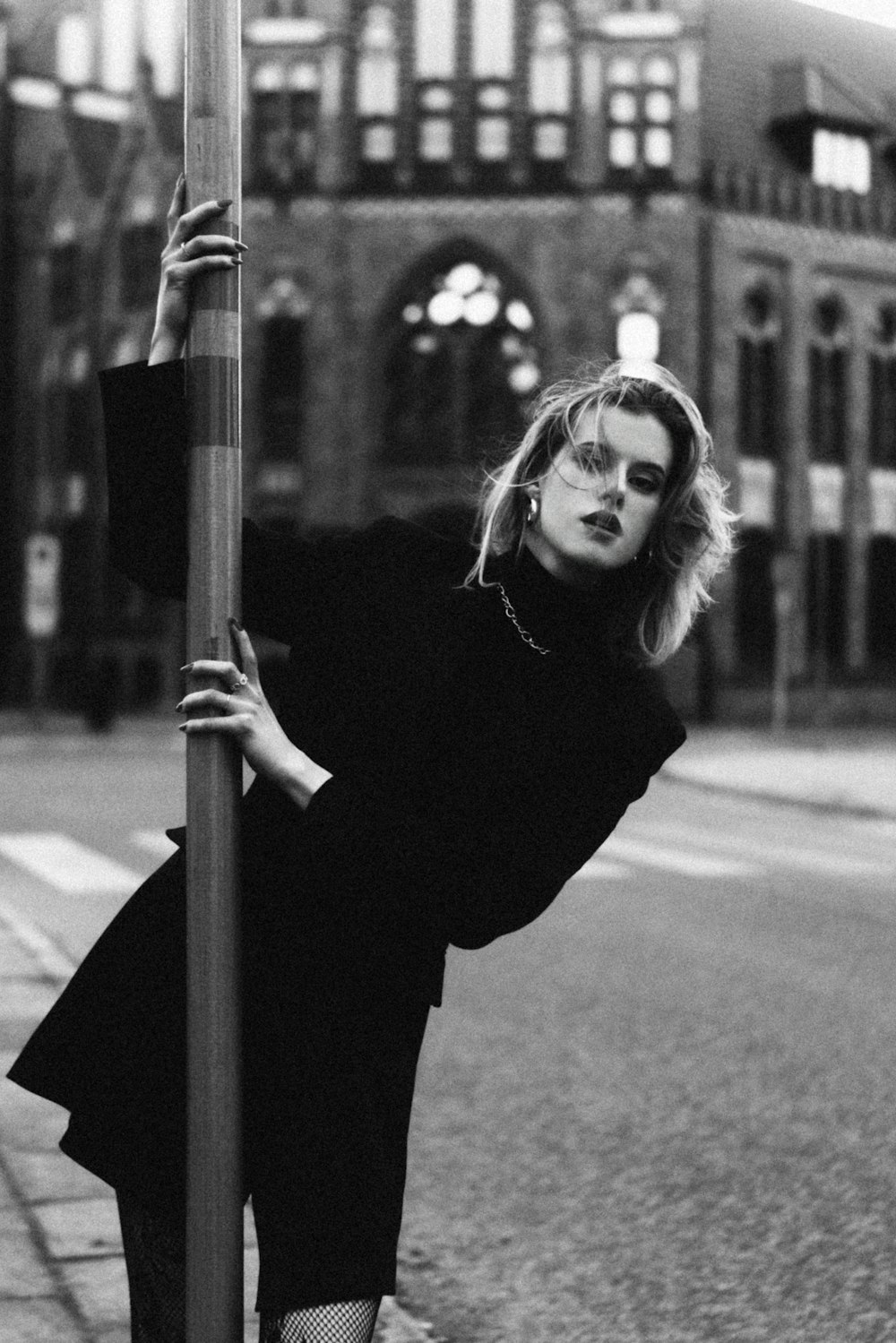 a black and white photo of a woman leaning on a pole