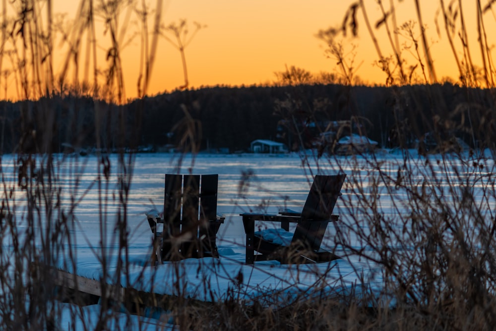 a couple of chairs sitting on top of a snow covered field