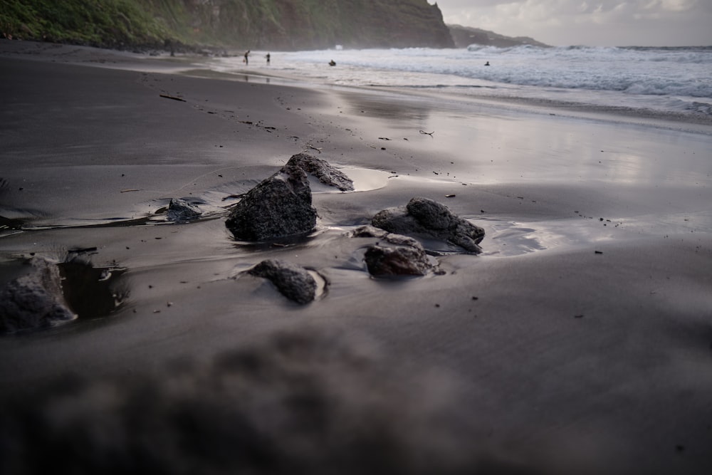 a beach with rocks on the sand and a cliff in the background