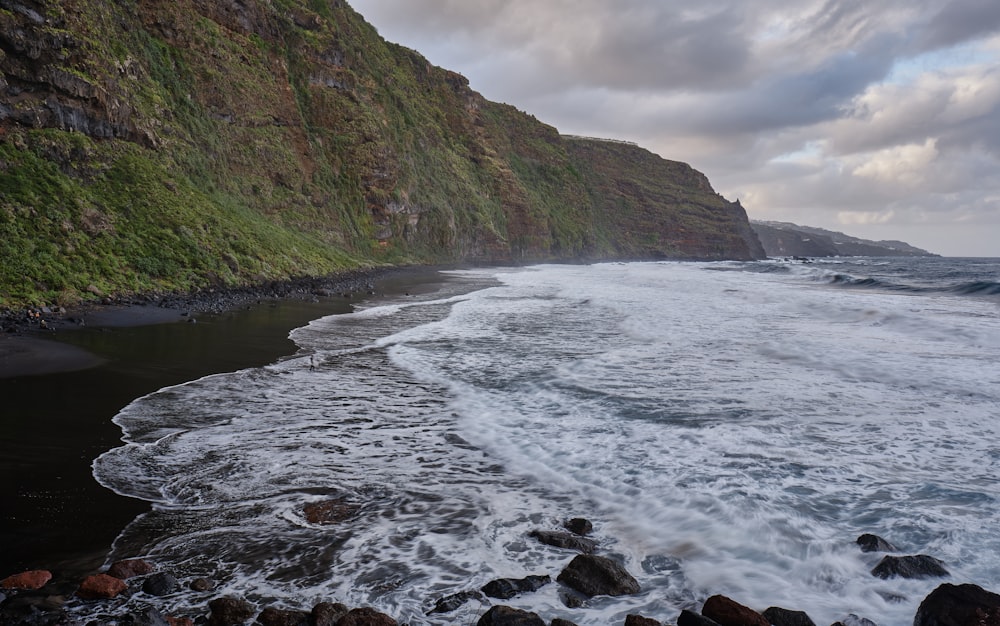 a rocky beach next to a cliff on a cloudy day