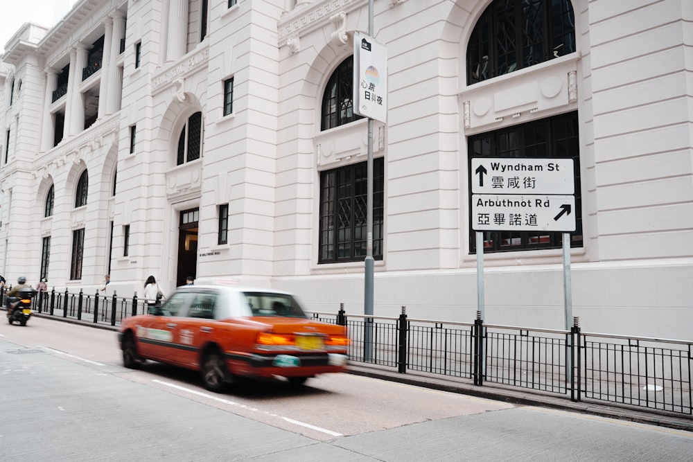 a red car driving past a tall white building