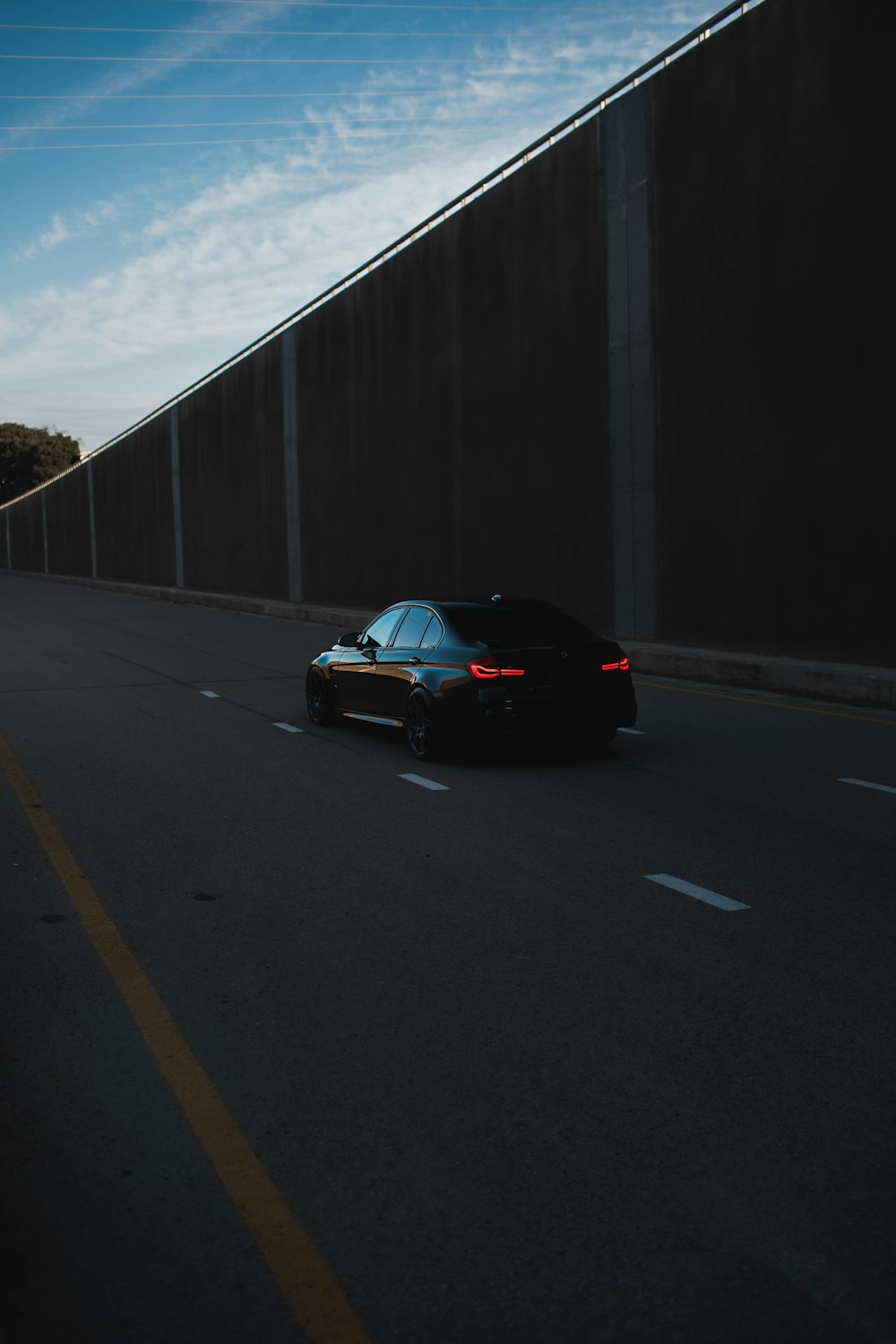 a black car driving down a street next to a tall wall