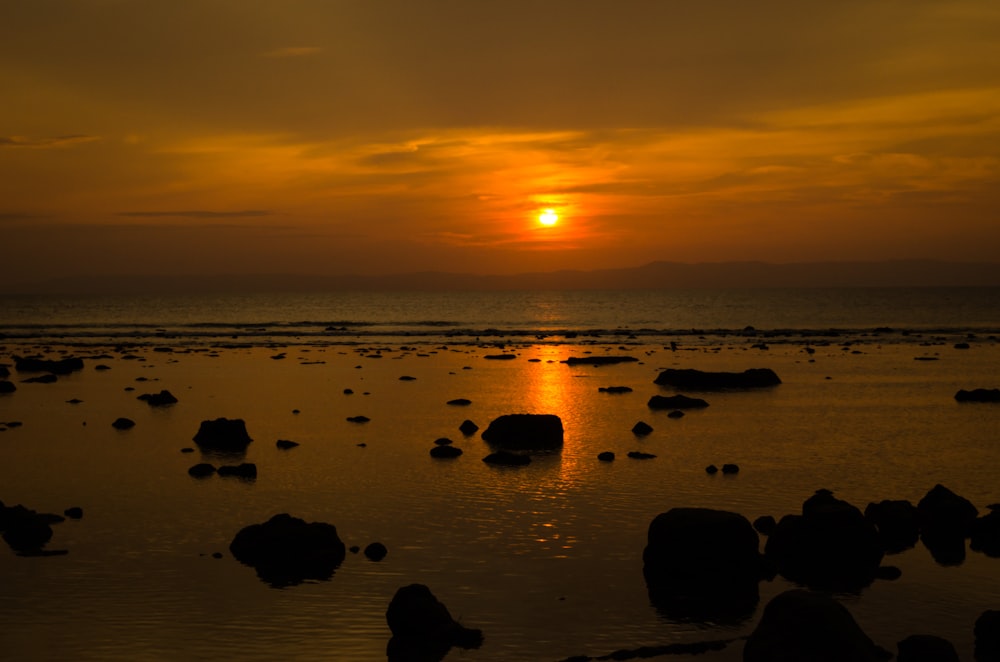 a sunset over the ocean with rocks in the foreground