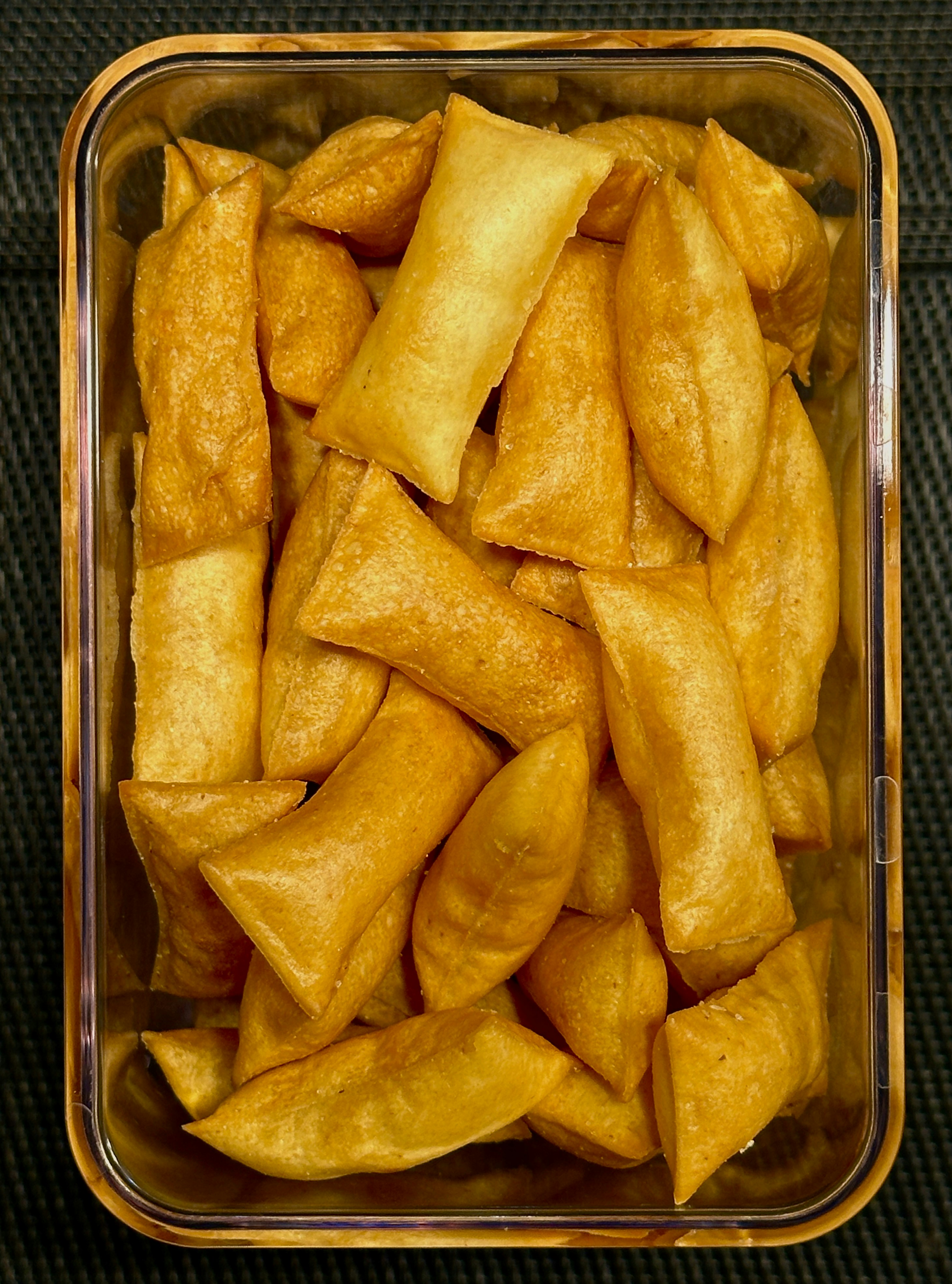 Golden fried snacks piled in a steel container at a market stall, moody evening light