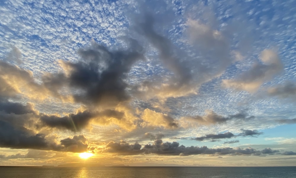 the sun is setting over the ocean on a cloudy day