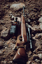 a rifle and a bottle of whiskey on a rocky ground