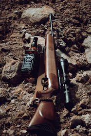 a rifle and a bottle of whiskey on a rocky ground