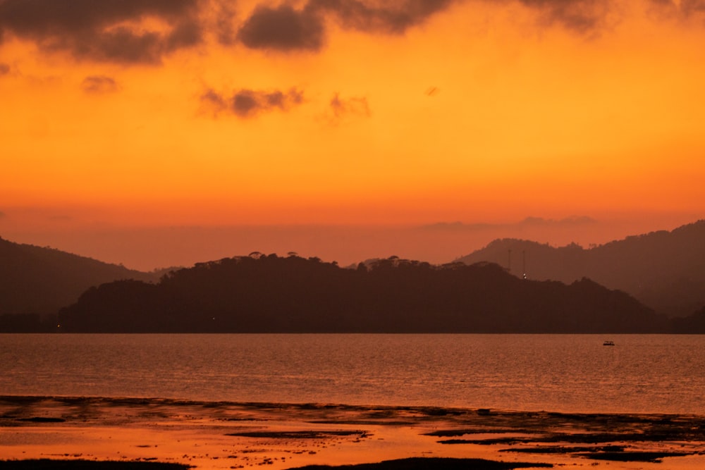 a sunset over a body of water with mountains in the background