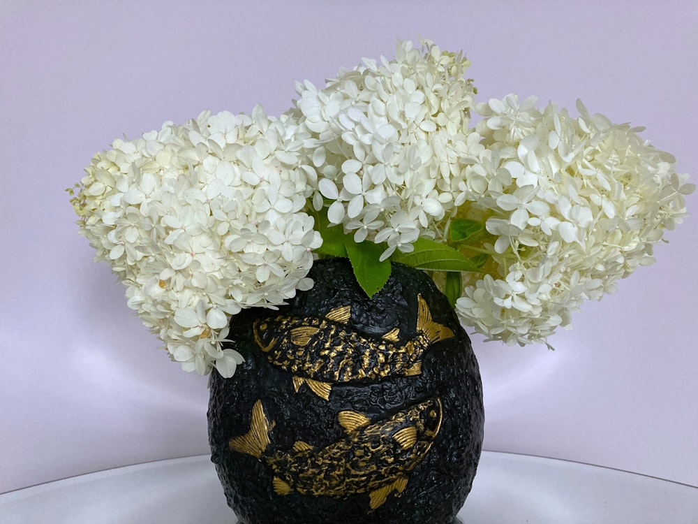 a black vase filled with white flowers on top of a table