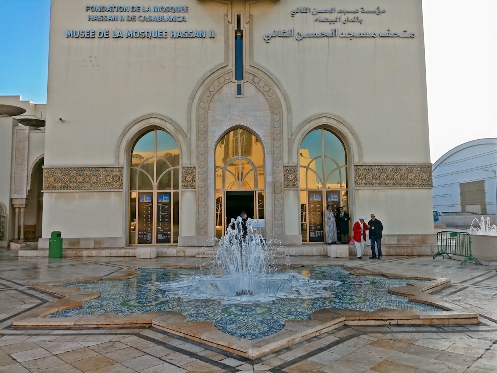 two people standing in front of a building with a fountain