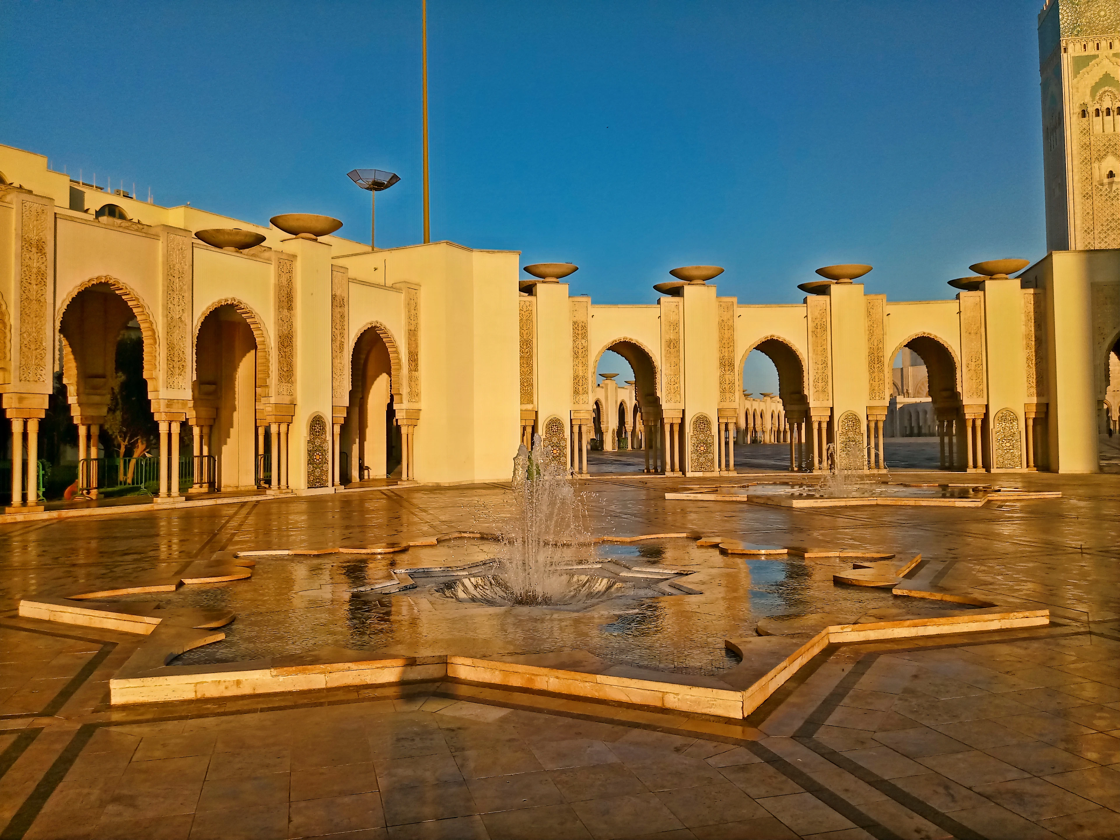 A star-shaped fountain in the Hassan II Mosque's arcaded courtyard, lit by warm afternoon light.