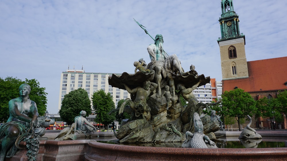 a fountain with statues and a clock tower in the background