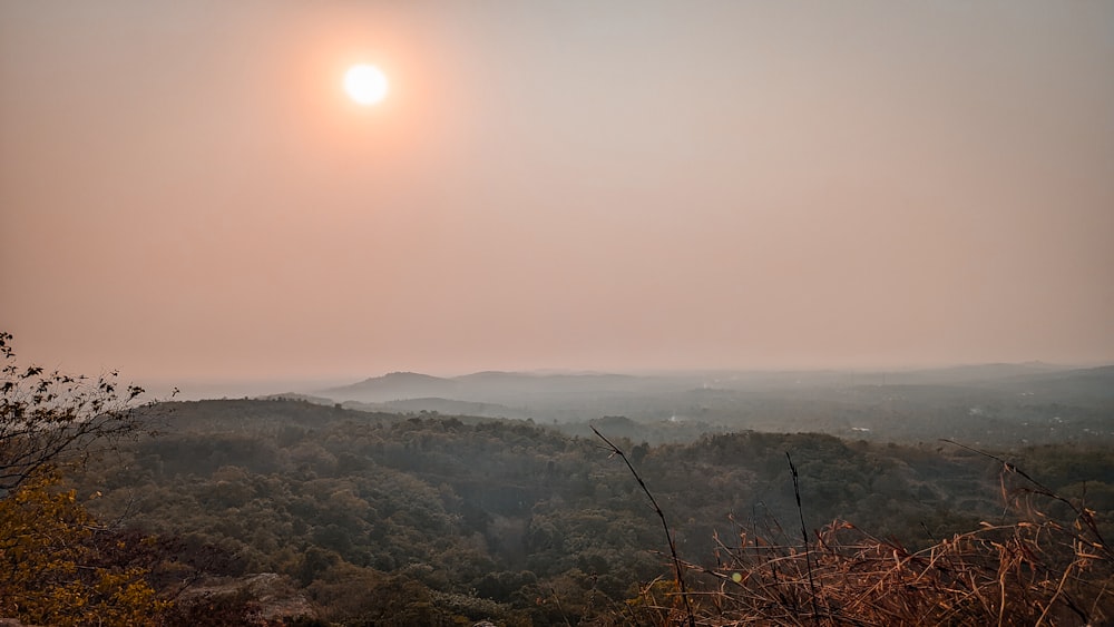 the sun is setting over the hills and trees