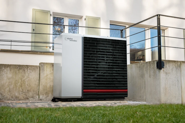 An outdoor heat pump unit on grass in front of a white house with a railing