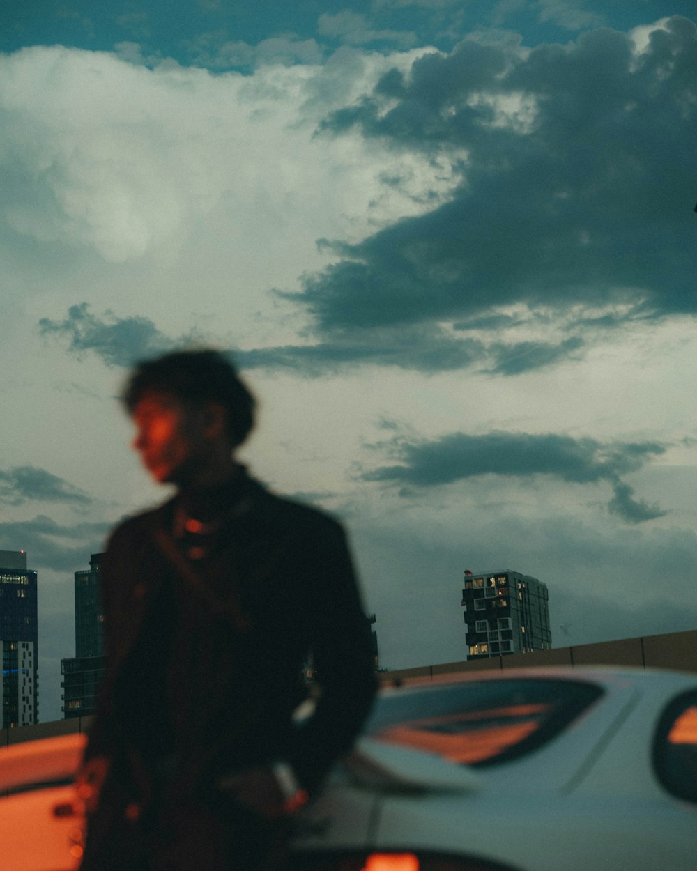 a man standing next to a white car under a cloudy sky