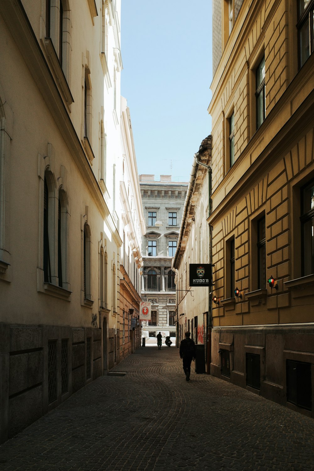 a couple of people walking down a street next to tall buildings