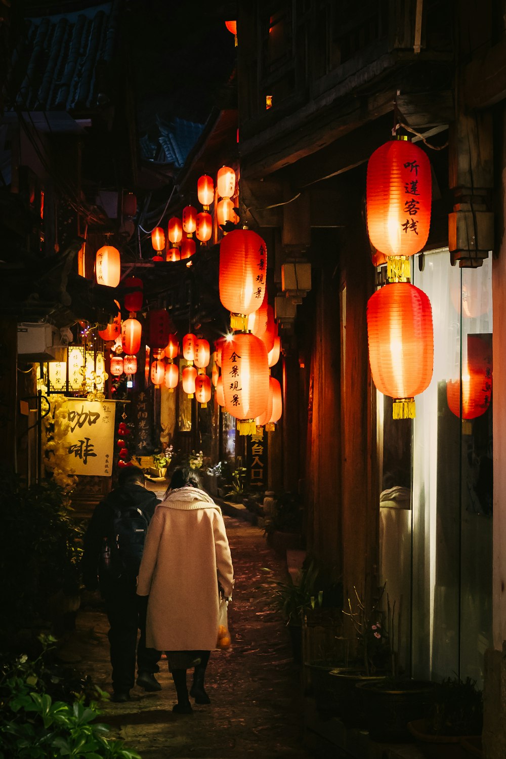 a couple of people walking down a street under lanterns