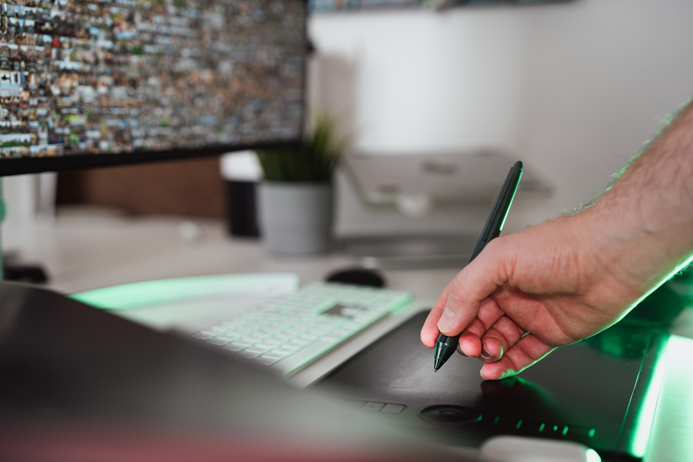 a hand holding a pen over a computer keyboard