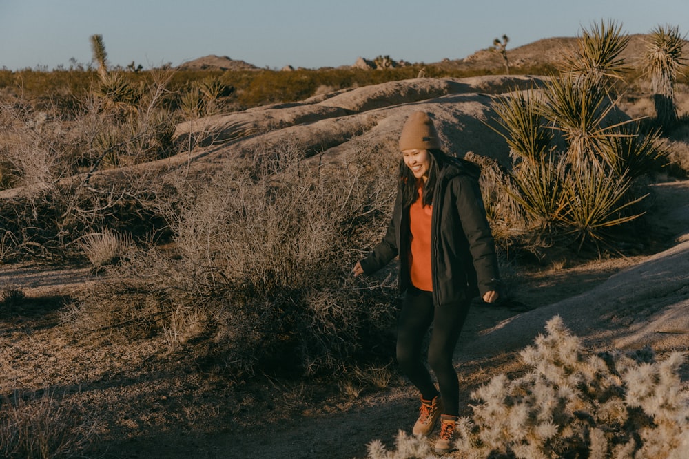 a woman in a red shirt and black jacket walking through a desert