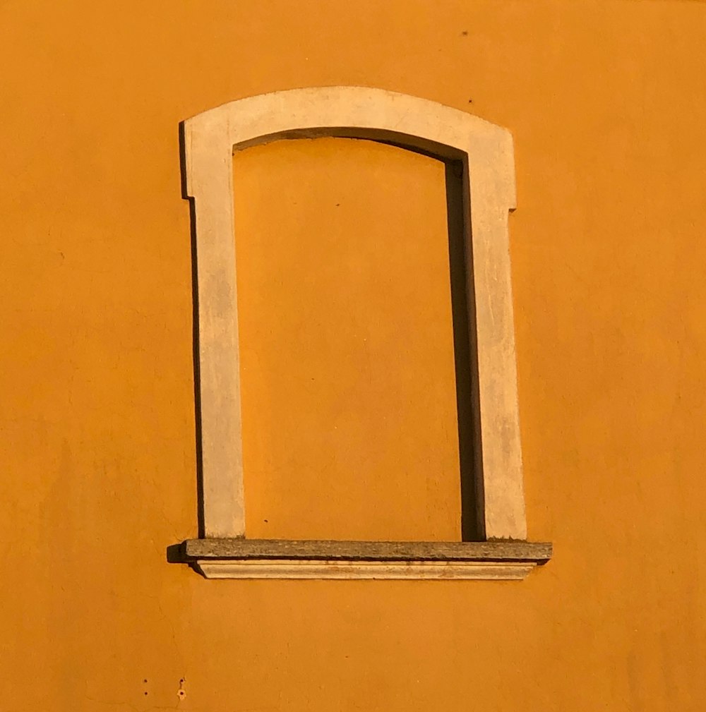 a yellow wall with a window and a cat sitting on the ledge