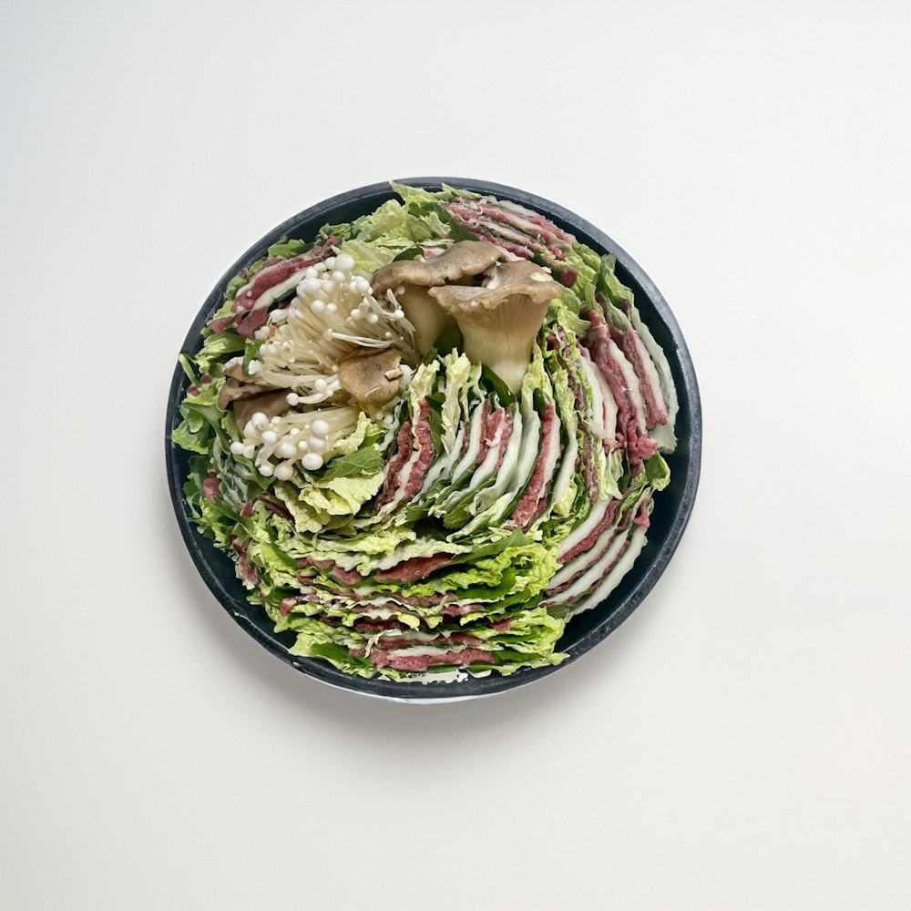 a bowl of lettuce and other vegetables on a white surface