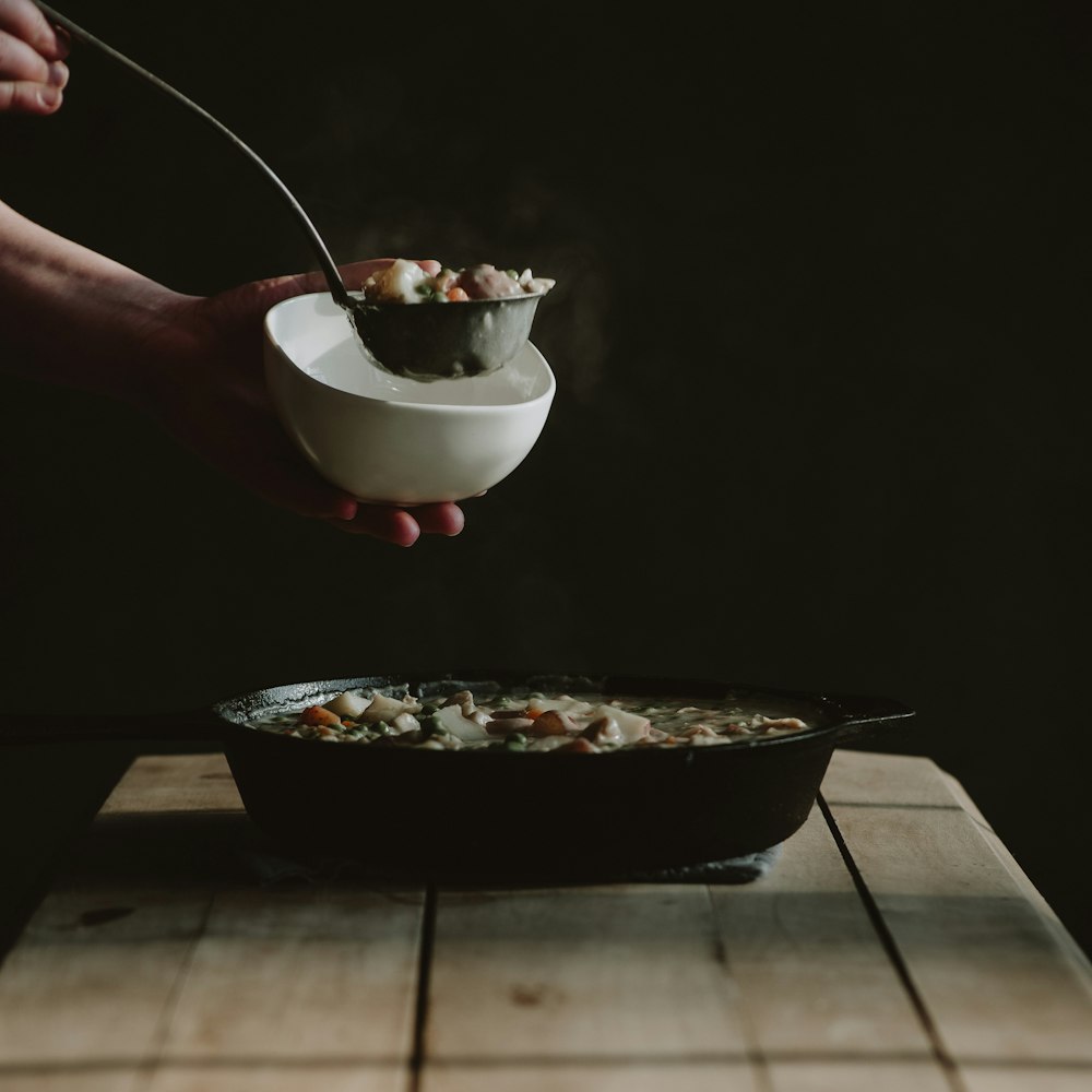 a person holding a spoon over a bowl of food