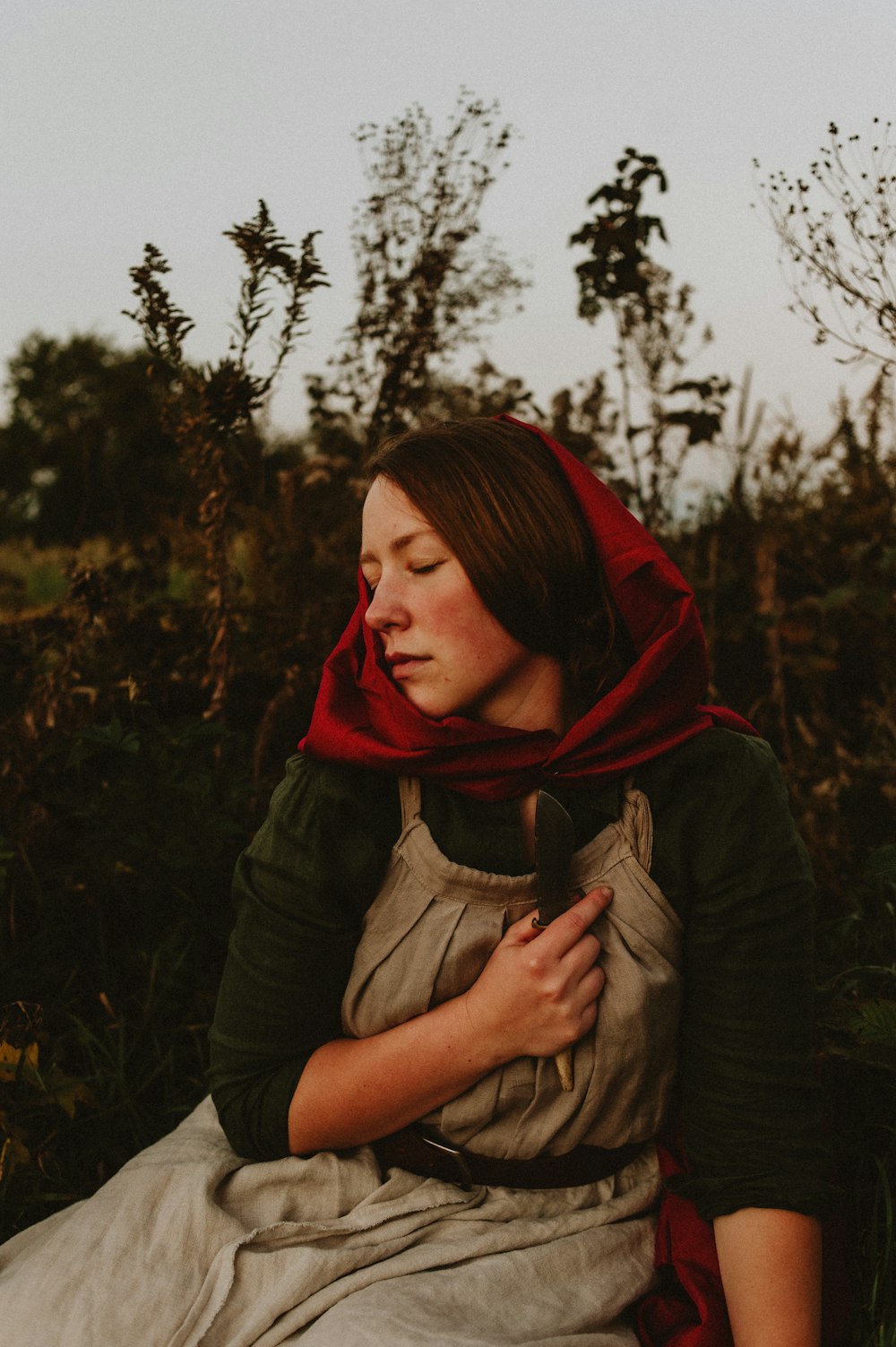 a woman sitting in a field with a red scarf around her neck
