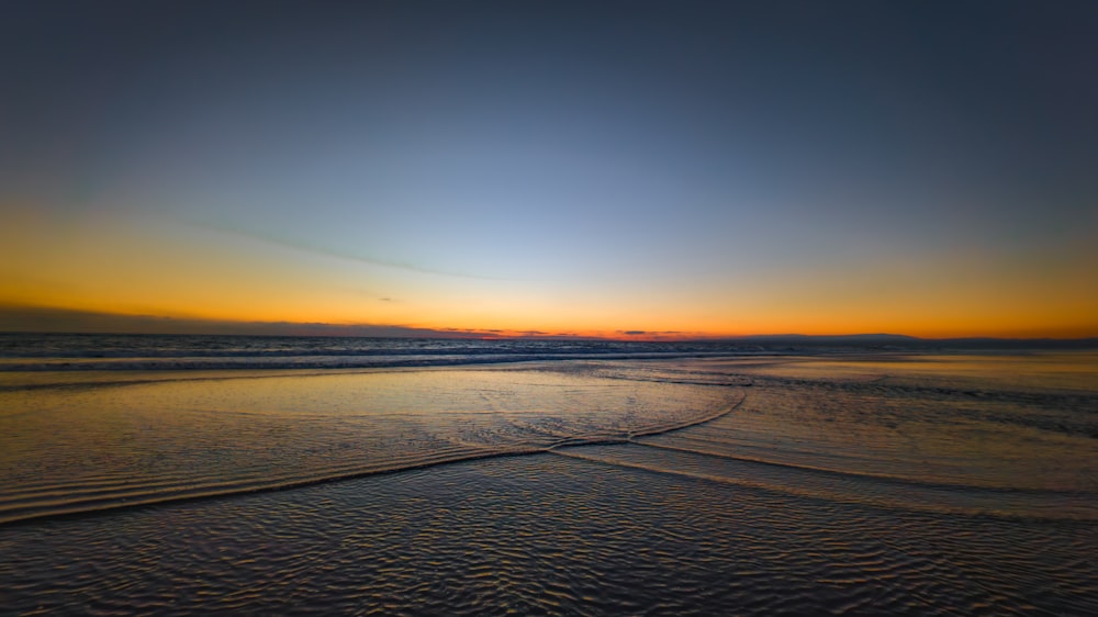 the sun is setting over the ocean on the beach