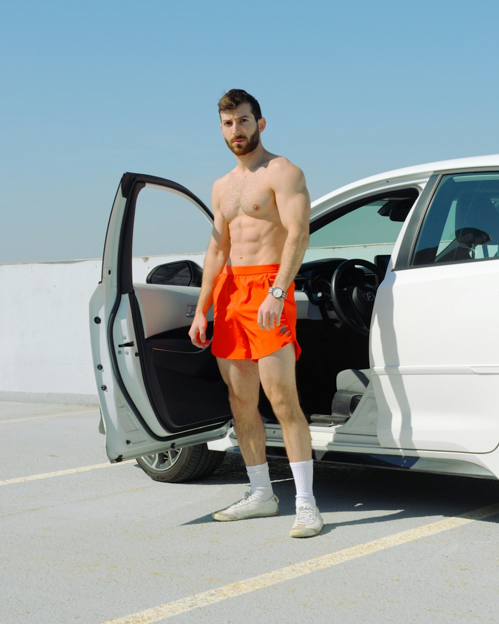 a man with no shirt standing in front of a car