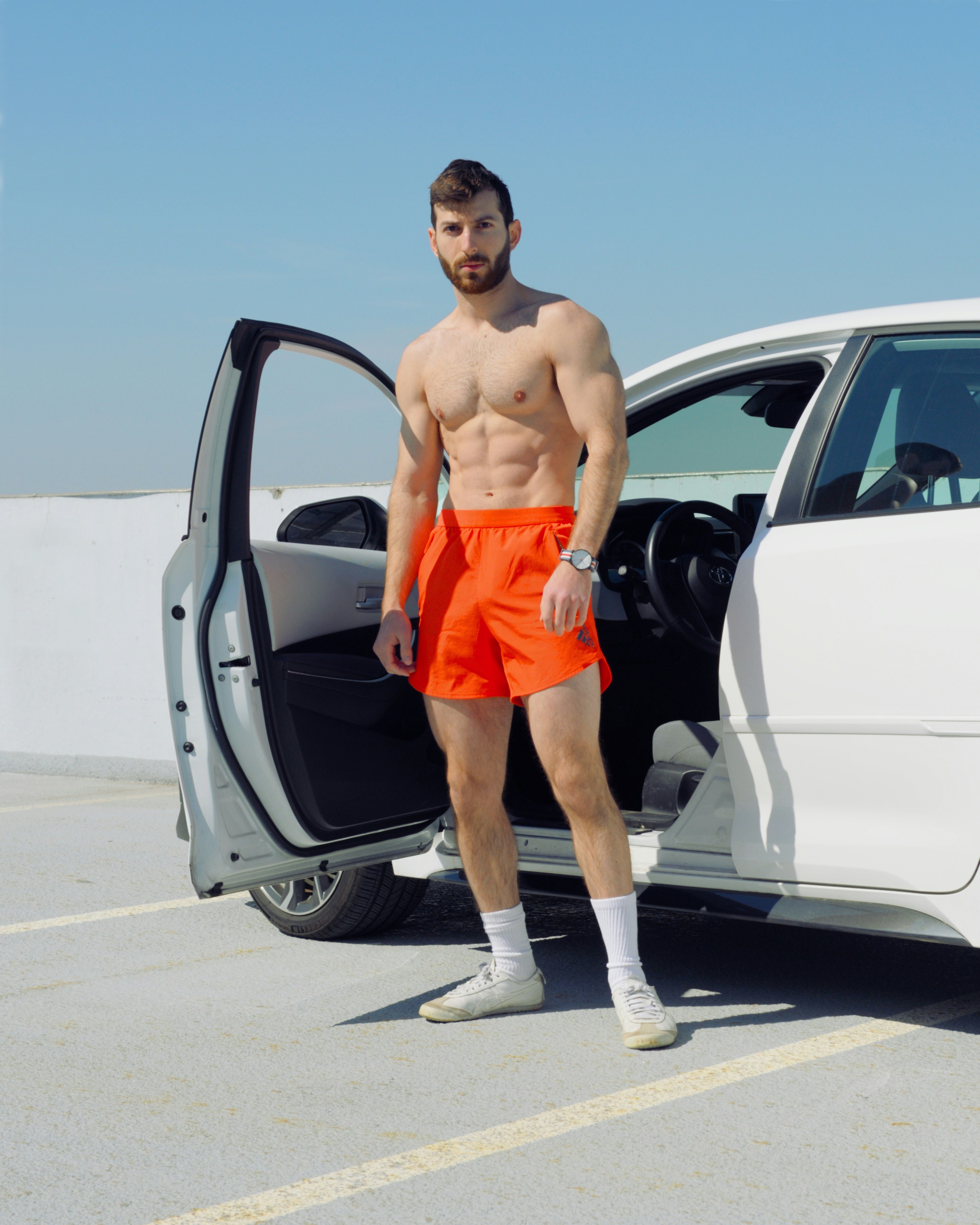 Ein Mann ohne Hemd steht vor einem weißen Auto