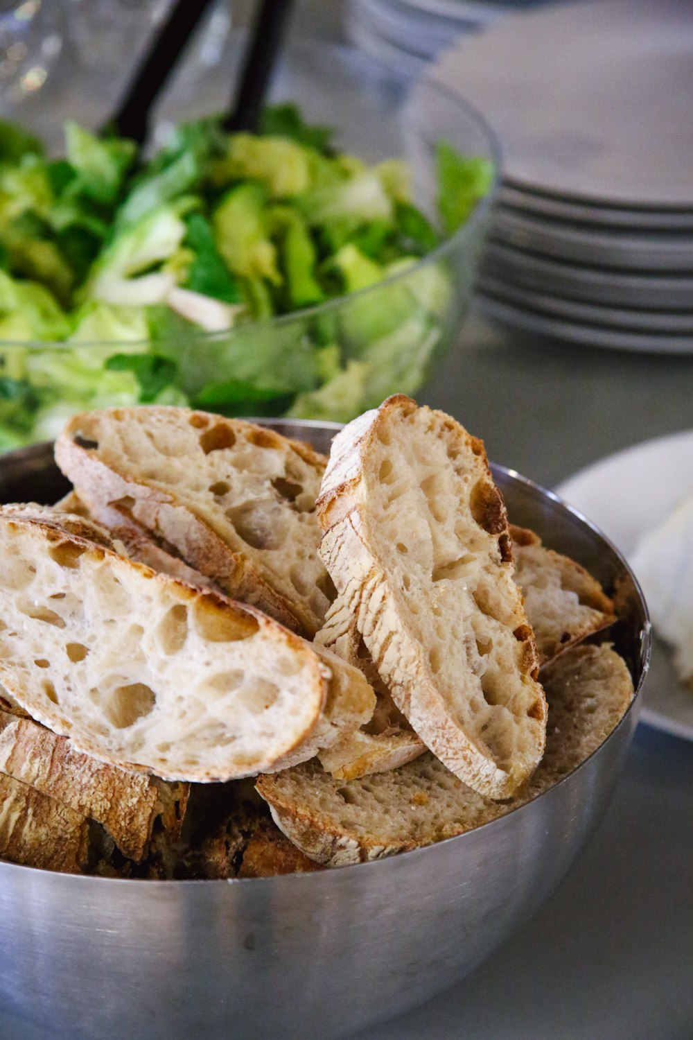 a metal bowl filled with sliced bread next to a salad