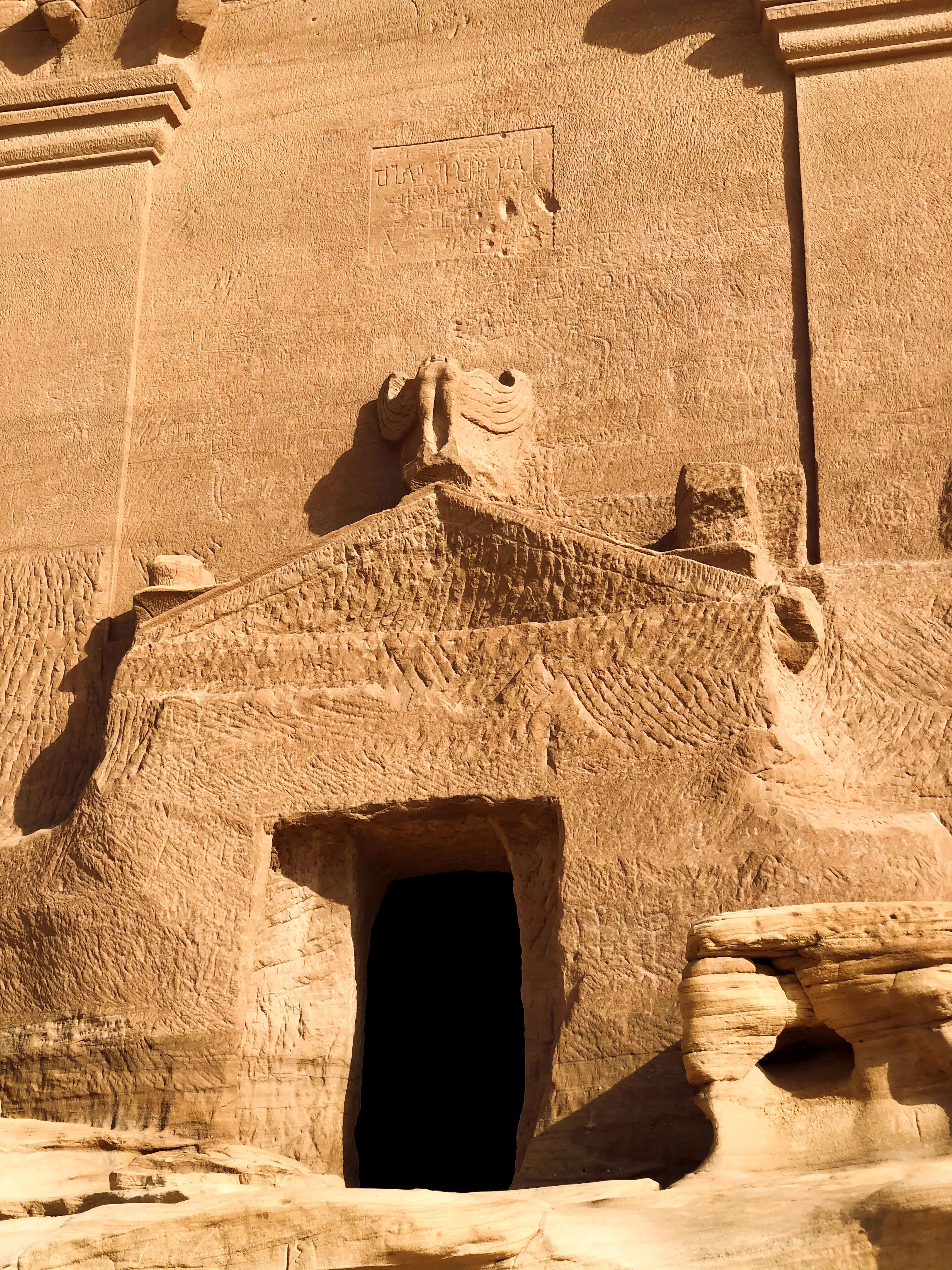 A carved Nabataean tomb facade at Hegra, AlUla, with an ornate crest above its dark doorway.