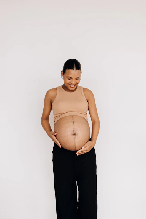 An expectant parent standing with hands resting on their pregnant belly