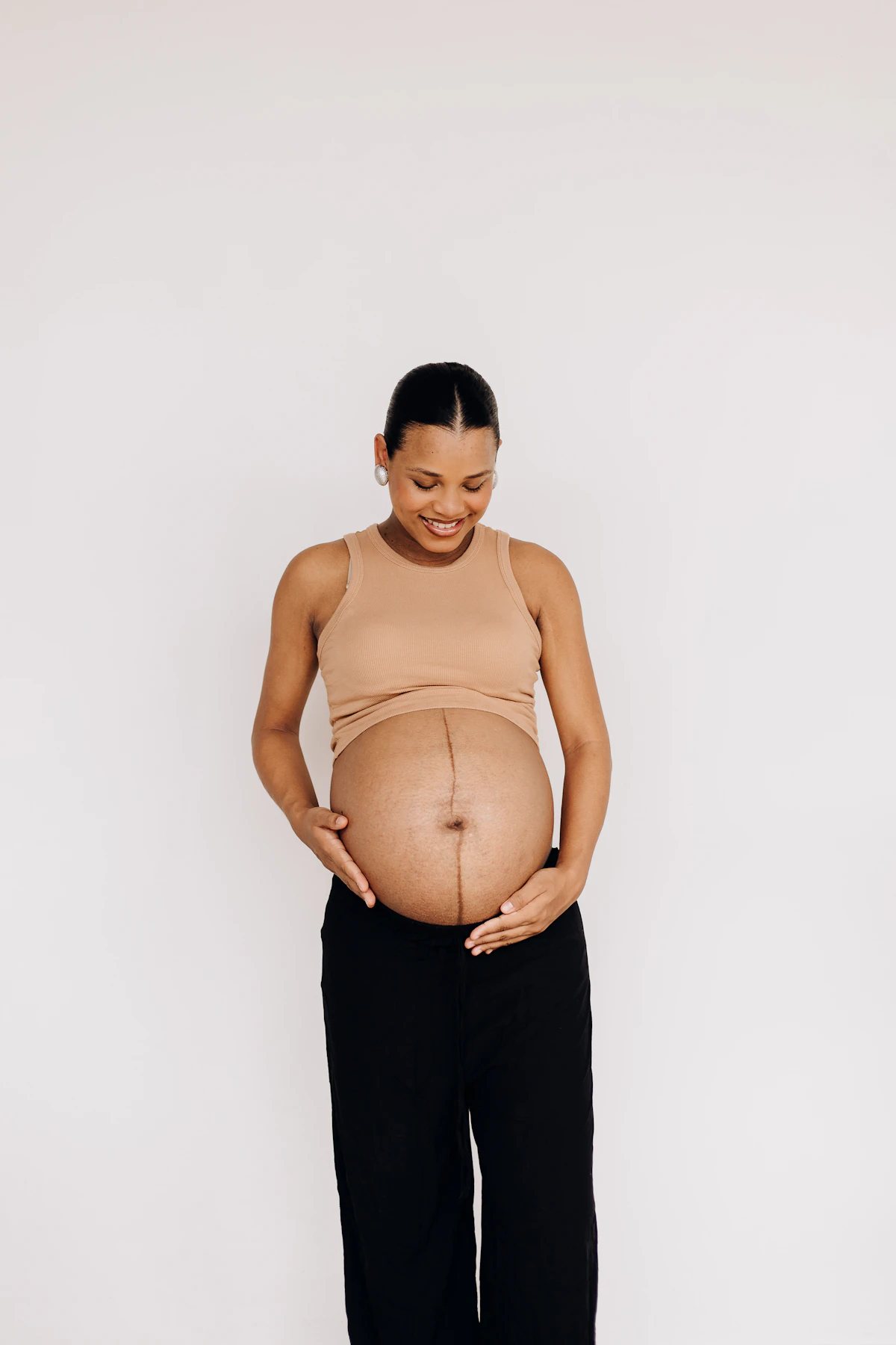 Smiling pregnant woman cradling her bump in soft daylight