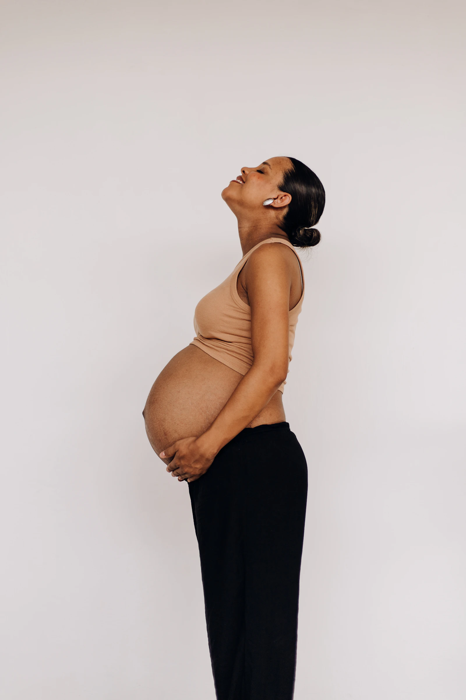 Pregnant woman in a tan top and black pants standing in profile
